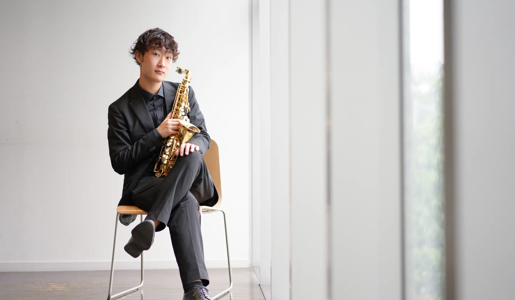 椅子に腰掛けサクソフォンを構える粟飯原叶翔